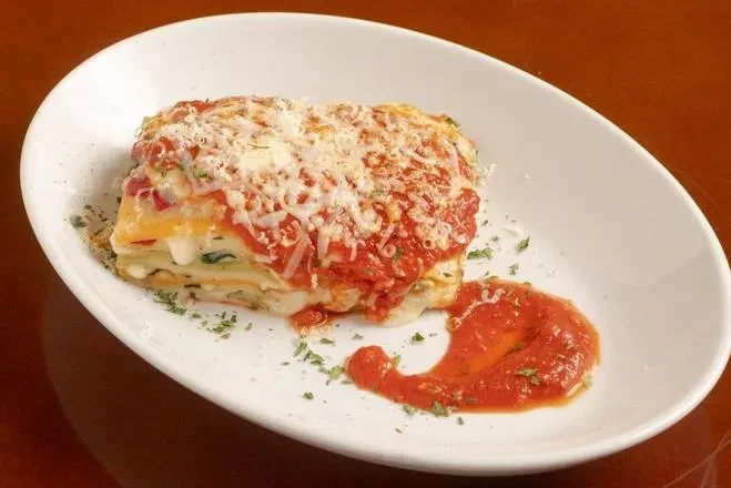 Layered lasagna with red sauce, grated cheese, and green herbs.