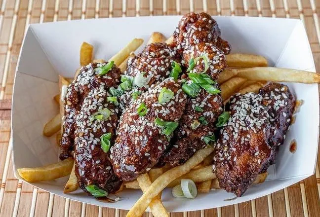Dark sauced chicken wings with sesame seeds and green onions over french fries.