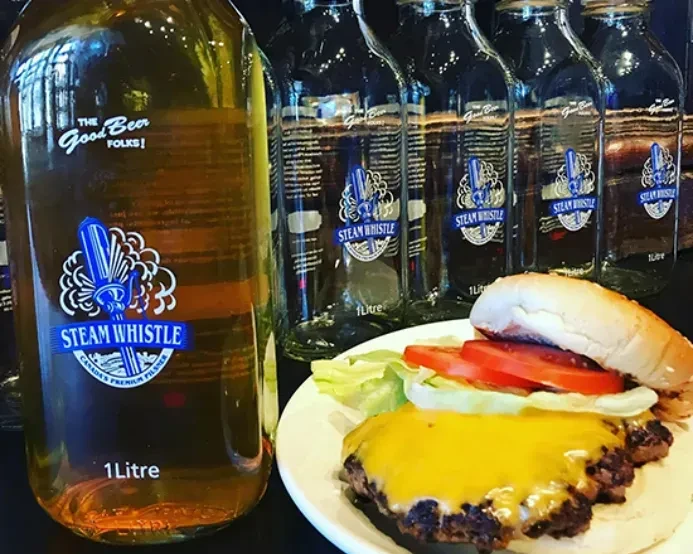 Open-faced cheeseburger with lettuce, tomato, and a Steam Whistle beer bottle.
