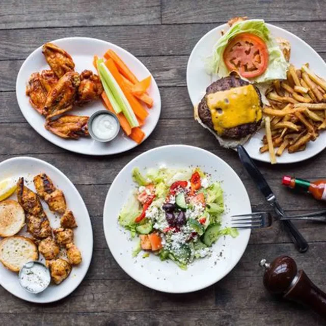 Rustic table with four plates: wings, burger, skewers, and salad.