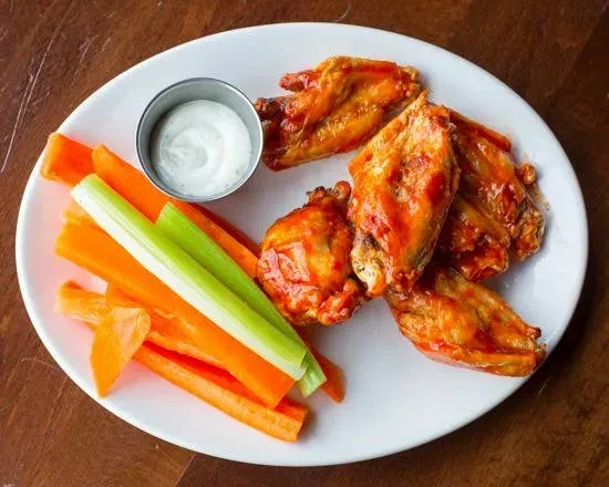 Glistening buffalo wings, celery, carrots, and creamy dipping sauce on a plate.