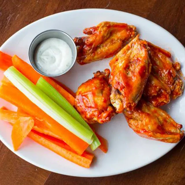 Orange-red buffalo wings, vegetable sticks, and dip on a white plate.