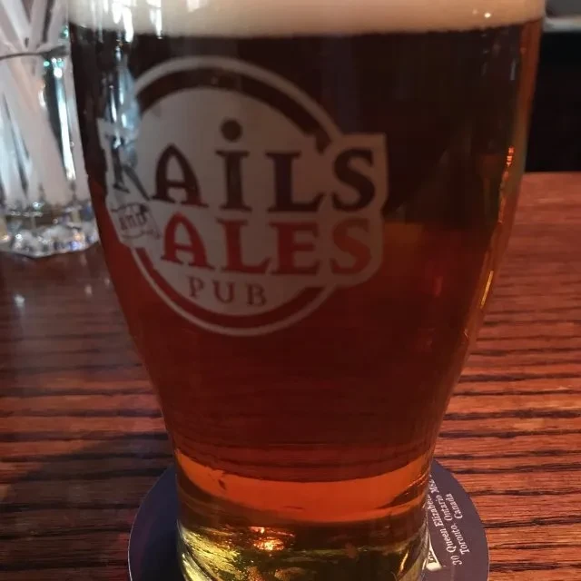Close-up of a pint of amber beer with a "RAILS & ALES PUB" logo.