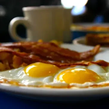 Two fried eggs, crispy bacon, hash browns, and steaming coffee.