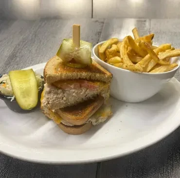Tuna melt sandwich with pickle, fries, and coleslaw on a white plate.