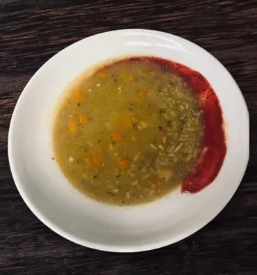 Close-up of yellow-green soup with carrots, herbs, and red garnish.