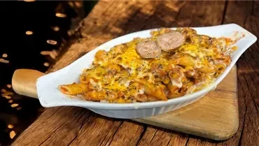Baked penne pasta with melted cheese and sausage on a wooden board.