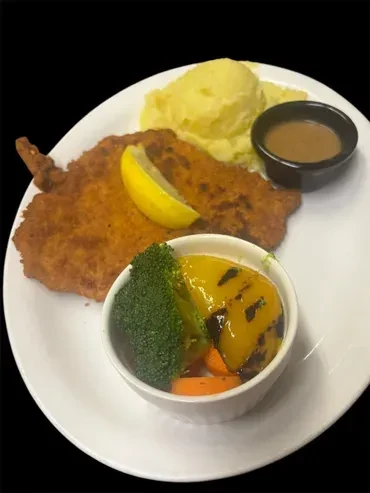 Crispy fried cutlet, mashed potatoes, gravy, and colorful vegetables on black.