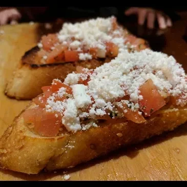 Golden bruschetta topped with tomatoes, crumbled feta, and grated Parmesan.