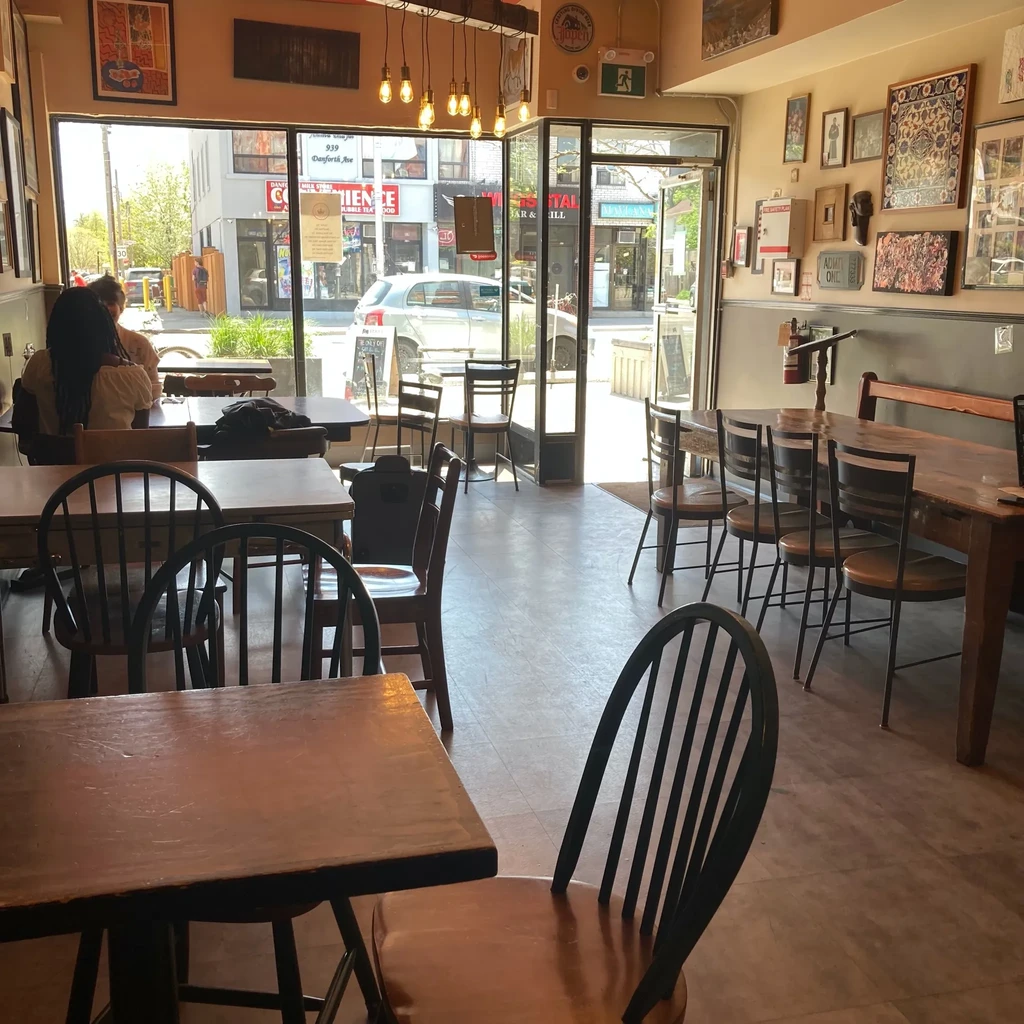 Restaurant interior with wooden tables, diverse art, and bright street view.