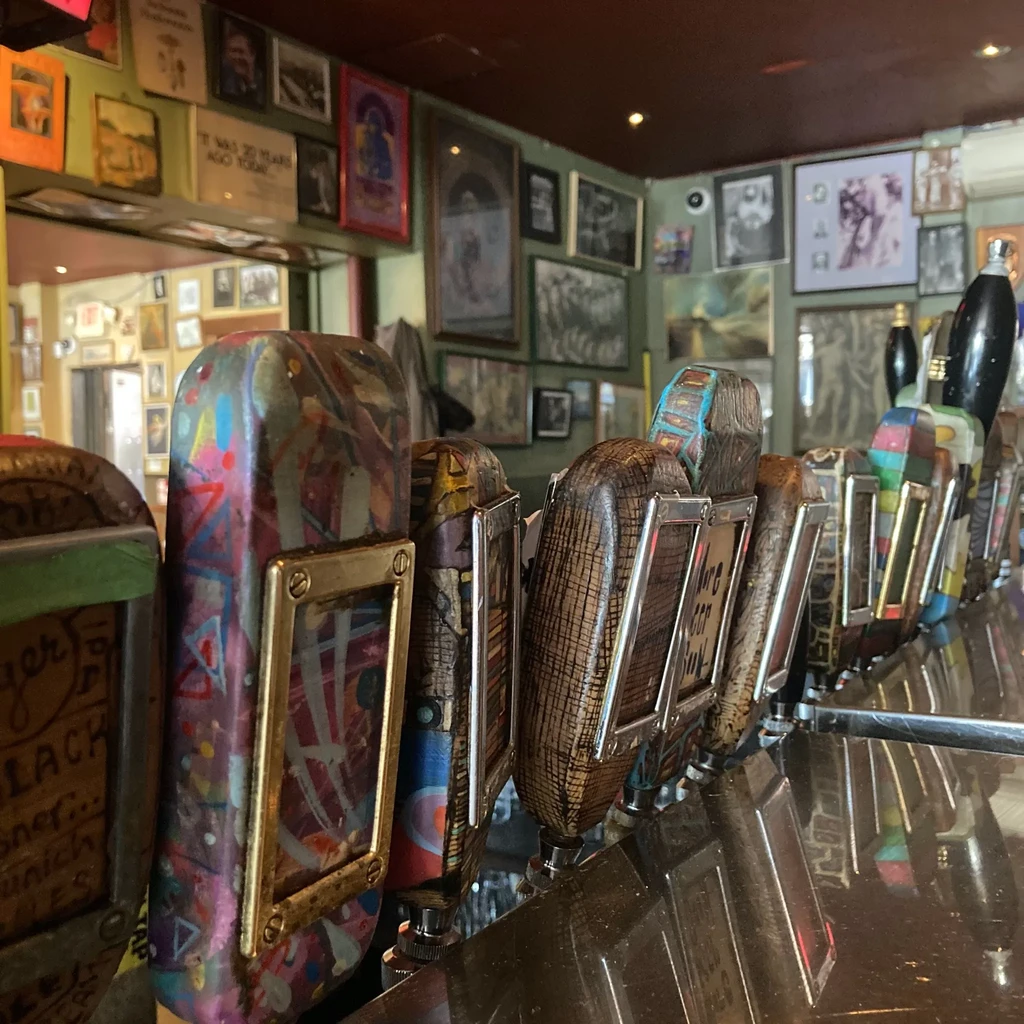 Varied, decorative beer tap handles foreground an eclectic art-filled bar.