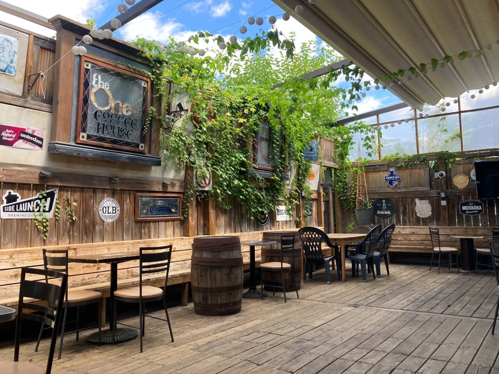 Rustic outdoor coffee house patio with vines, seating, and brewery signs.