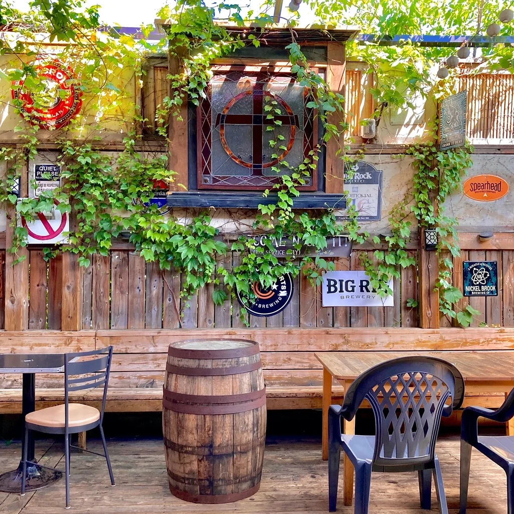 Rustic outdoor beer garden with barrel, vines, and brewery signs.