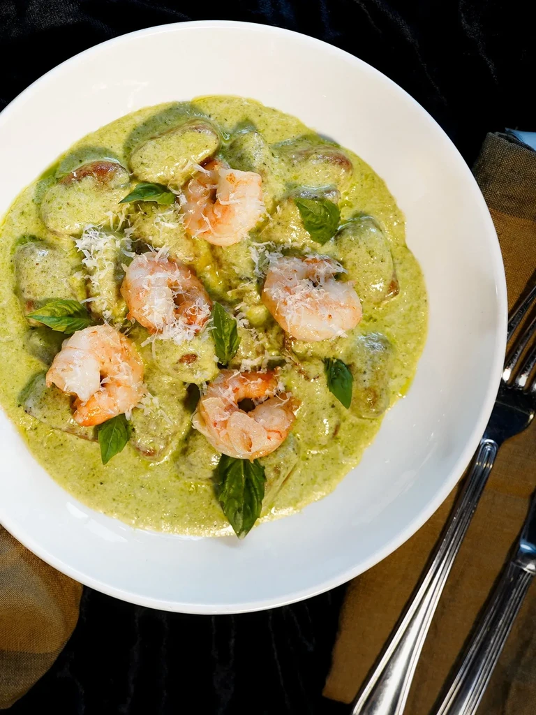 Overhead: Gnocchi with green sauce, shrimp, grated cheese, and basil.