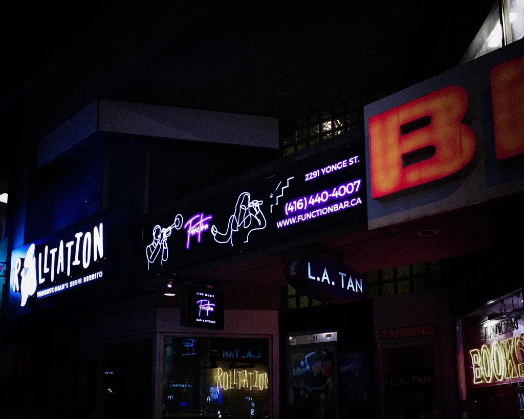 Bright neon signs for RollTation, Function Bar, and L.A. Tan at night.