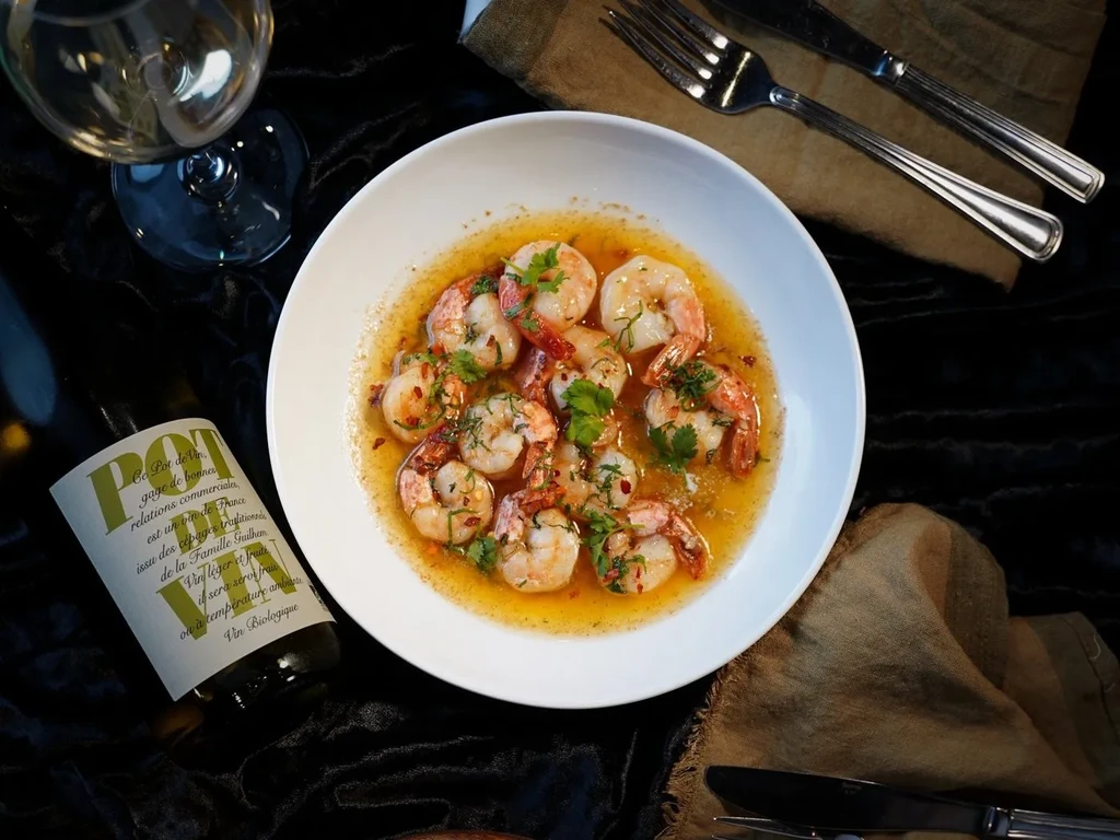 Overhead: Shrimp in orange sauce, Pot de Vin, wine glass, and cutlery.