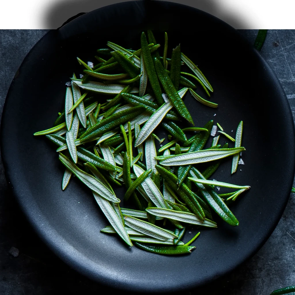 Fresh rosemary leaves and sea salt in a black bowl.