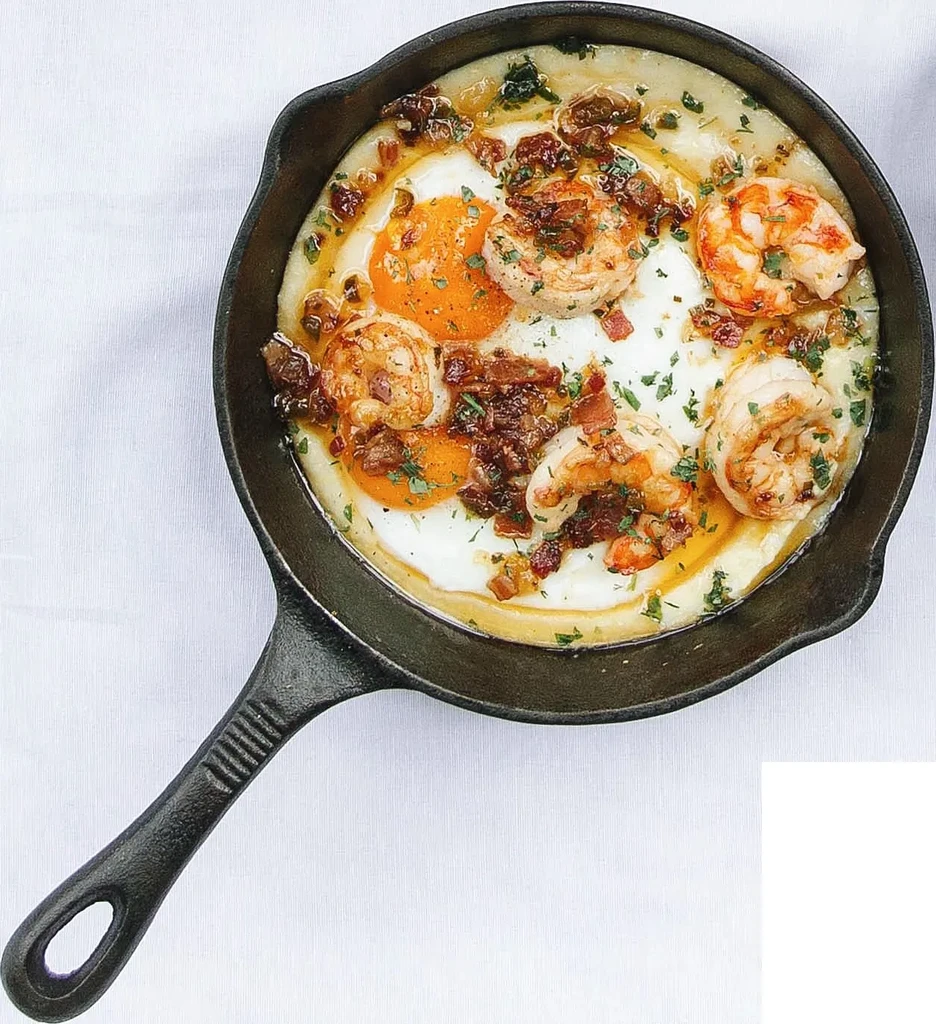 Cast iron skillet with creamy grits, shrimp, sunny-side eggs, and herbs.