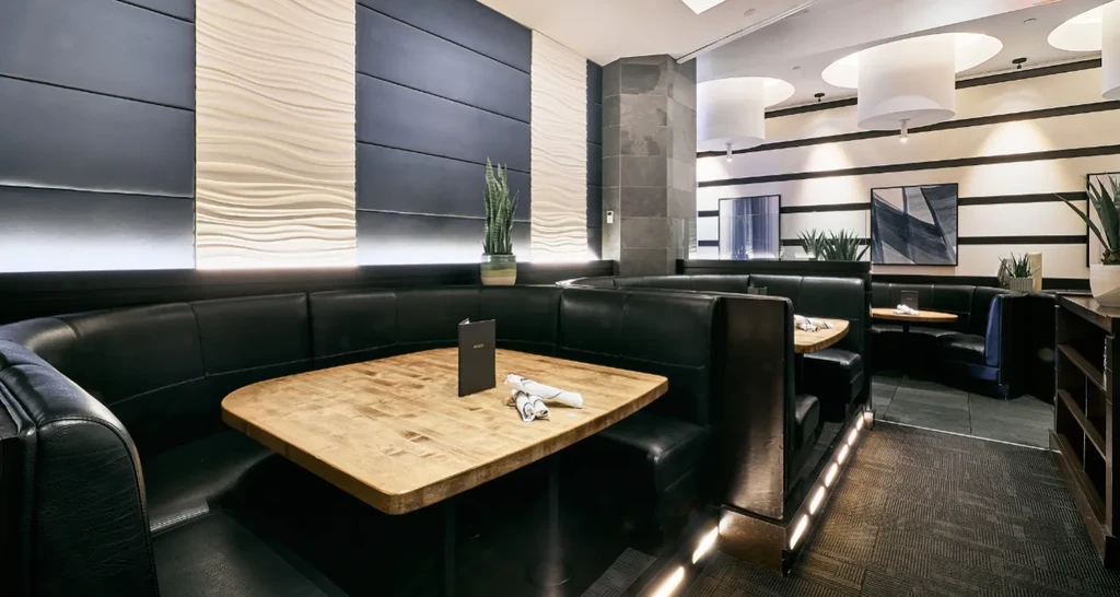 Empty modern restaurant with dark booths, light tables, and inviting lighting.