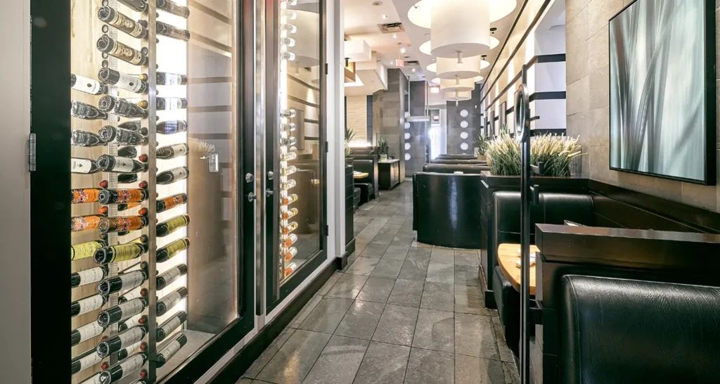Modern restaurant interior with a lit wine display and empty leather booths.