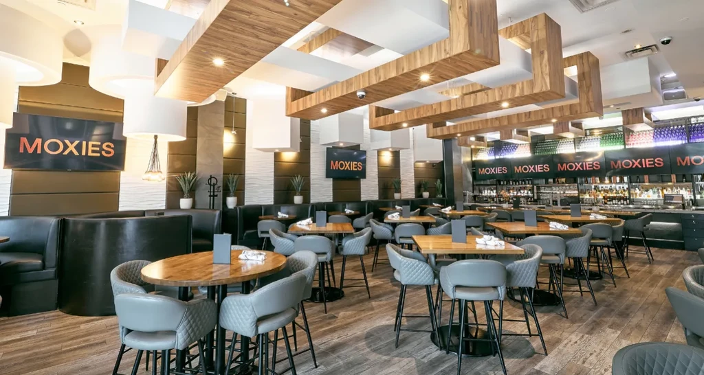 Modern upscale MOXIES restaurant interior with dining area and illuminated bar.