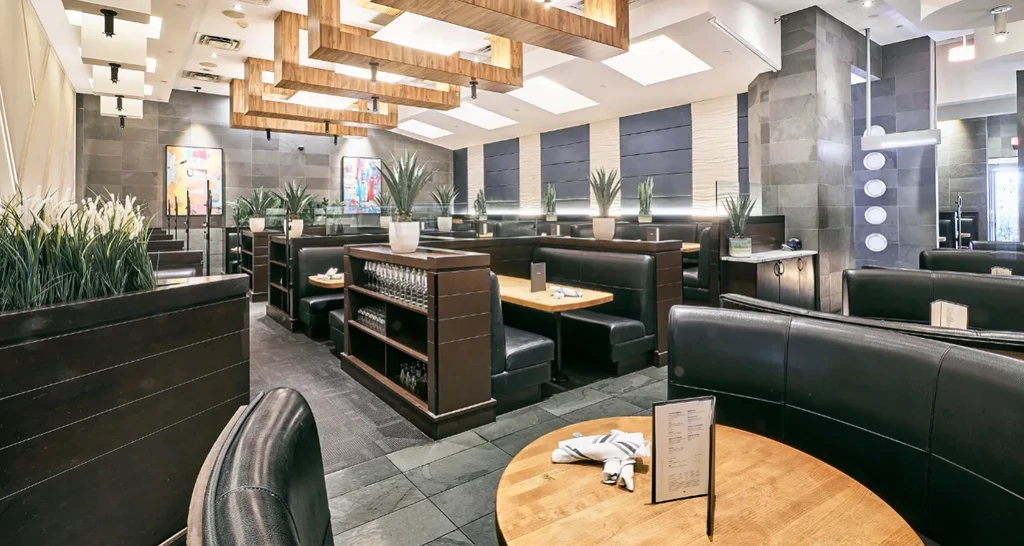 Modern restaurant interior with dark booths, decorative wooden beams, and plants.