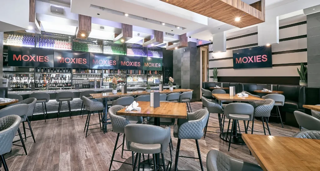 Modern restaurant and bar interior featuring dining area and 'MOXIES' signs.