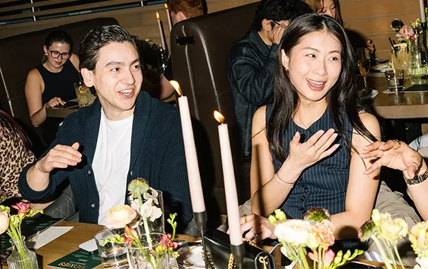 Smiling man and woman at a dim restaurant table with candles and flowers.