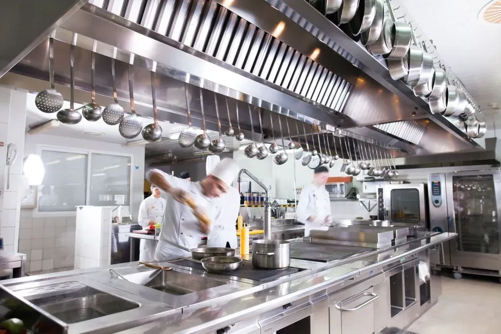 Chefs cooking in a bustling professional kitchen with stainless steel equipment.
