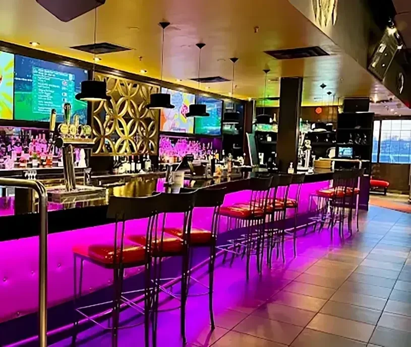 Vibrant bar with purple LED lights, top hat lamps, TVs, and stools.