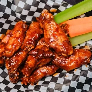 Piled, saucy chicken wings in a container with celery and carrot sticks.