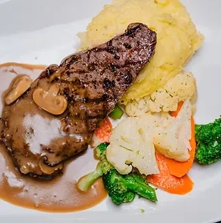 Grilled steak with gravy, mashed potatoes, and vibrant steamed vegetables.