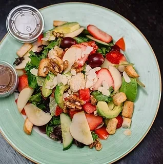 Vibrant salad with strawberries, avocado, nuts, cheese on a mint green plate.