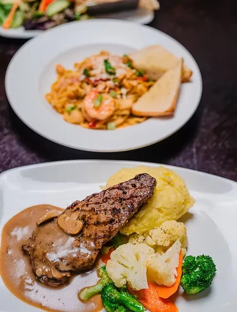 Two plates of professionally plated steak with sides and pasta.