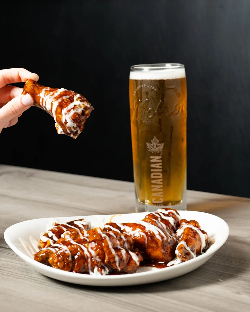 Sauced chicken wings, one held, with Molson Canadian beer.