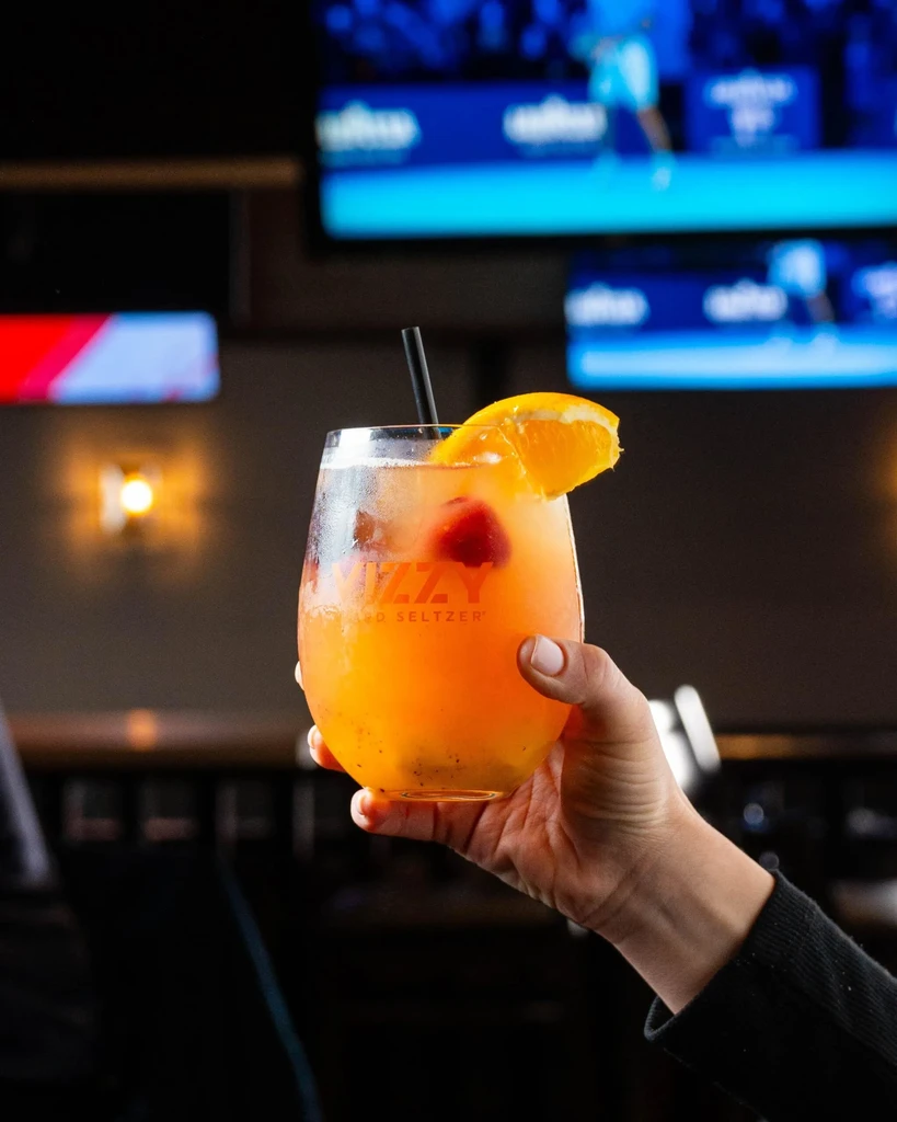 A hand holds a fizzy hard seltzer garnished with orange and berries.