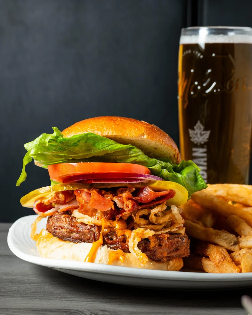 Close-up of a stacked burger, golden fries, and dark beer.
