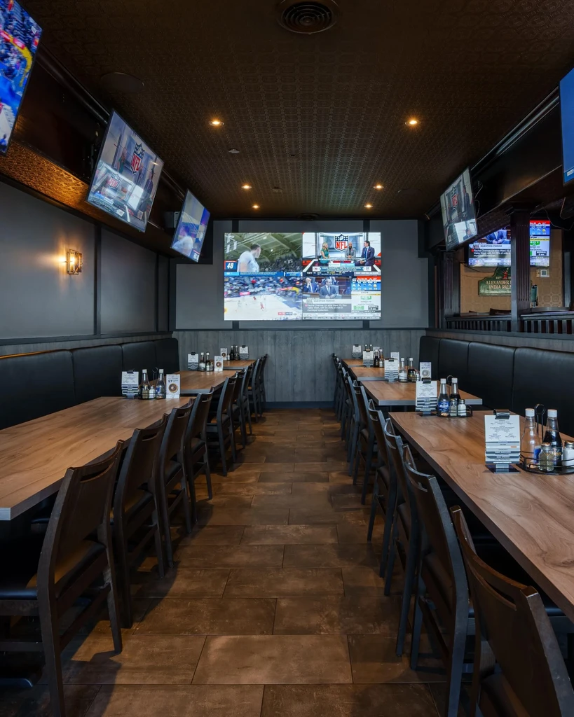 Empty modern sports bar with tables, chairs, and multiple active sports screens.