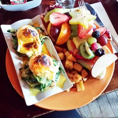 Plate of Eggs Benedict, fruit platter, and roasted potatoes.