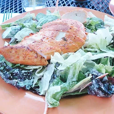 Large grilled chicken salad with creamy dressing on an orange plate.
