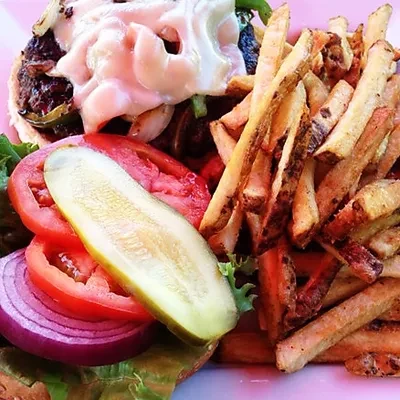 Close-up of a burger with pink sauce, pickle, and rustic fries.