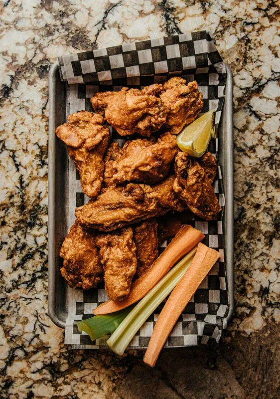 Fried chicken wings with lemon, carrot, and celery sticks in a tray.