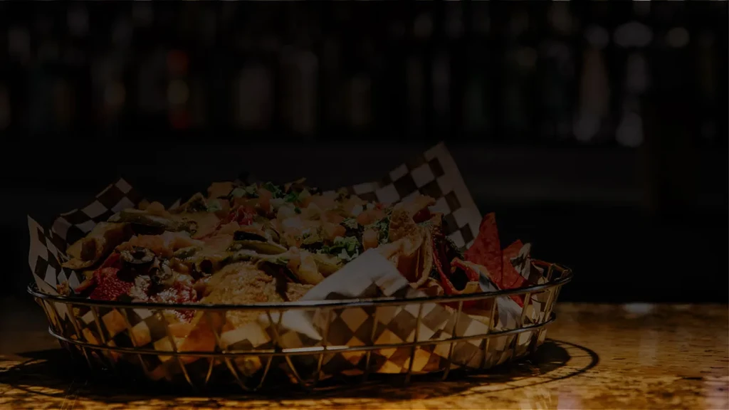 Piled high nachos in a mesh basket with cheese, tomatoes, and greens.