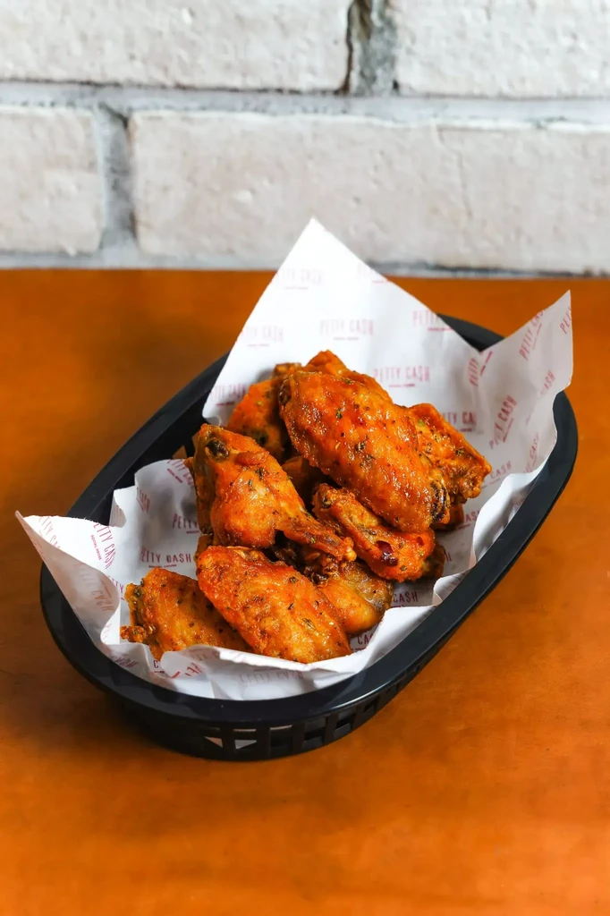 Golden chicken wings with herbs in a black basket on a wood table.