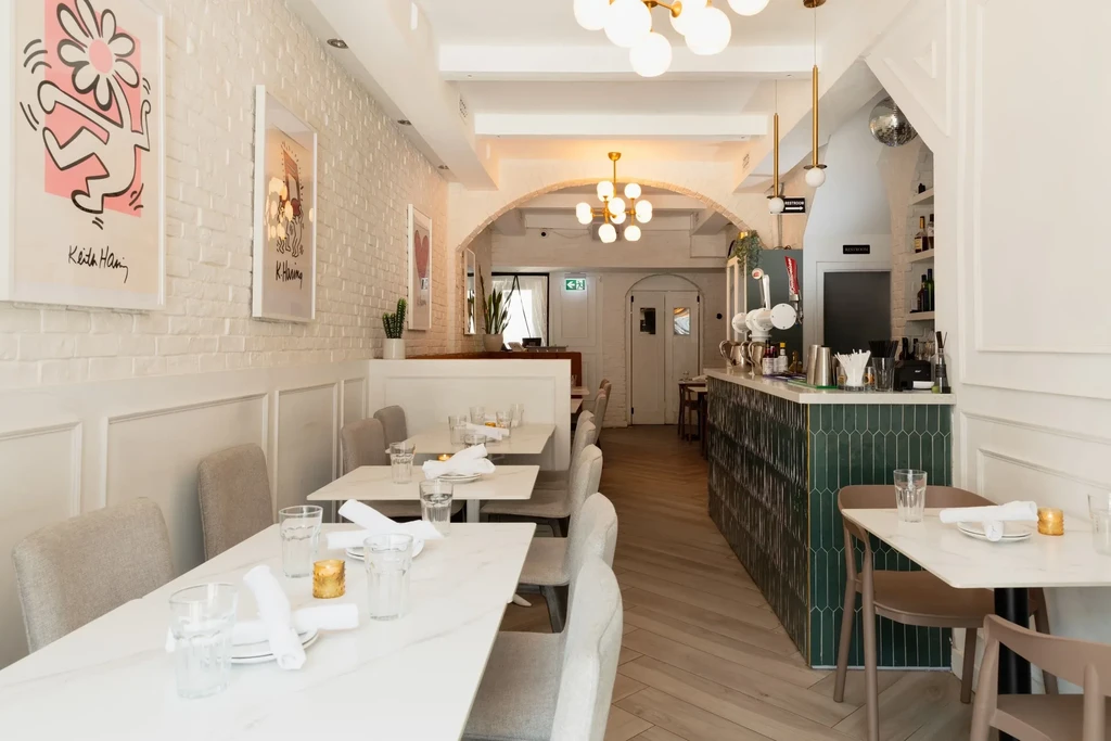 Empty modern restaurant interior with green bar, marble tables, and Haring art.