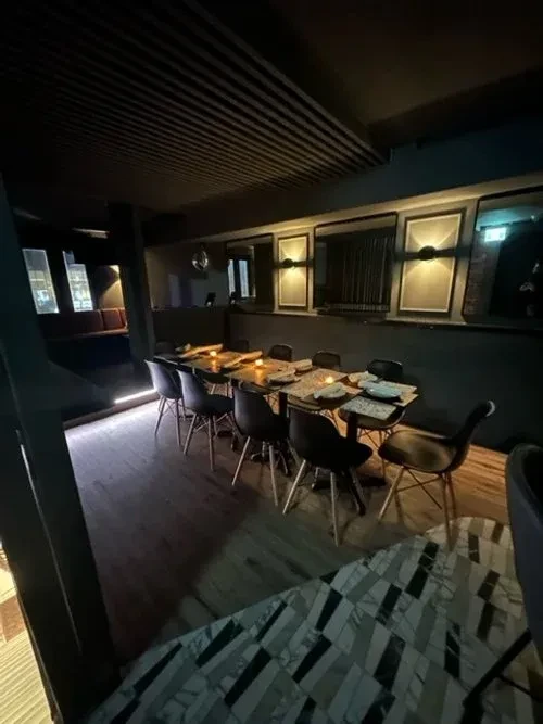 Dimly lit modern restaurant interior with long dining tables and chairs.