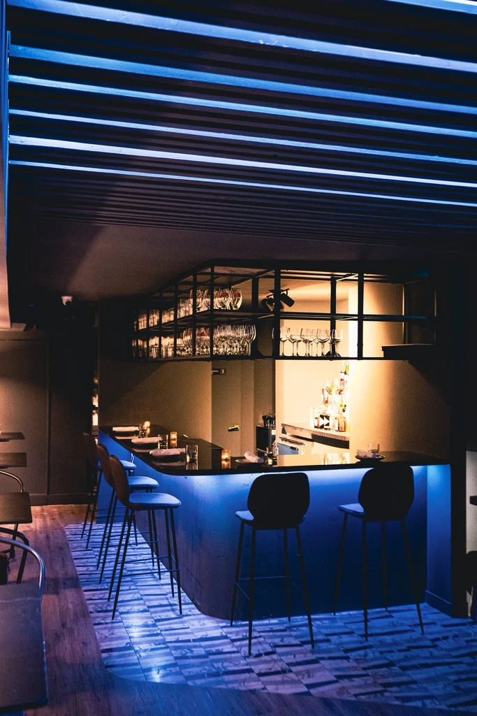 Empty, modern bar with blue under-lit counter and liquor bottles.