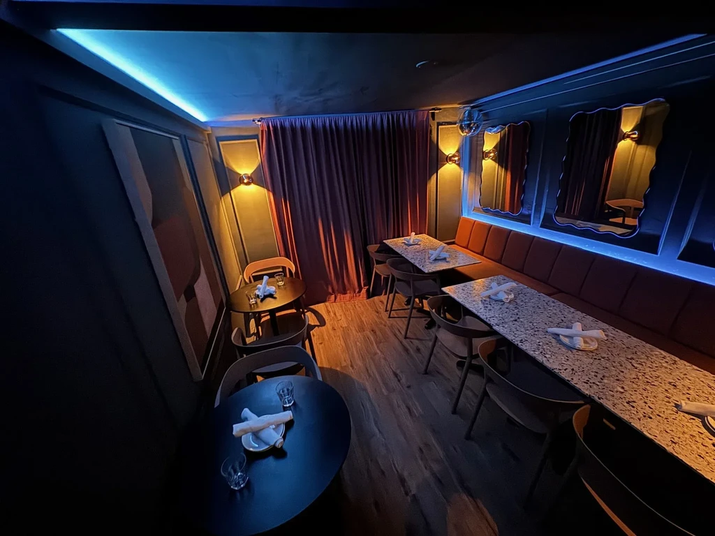 Dimly lit restaurant interior with banquette seating, tables, and abstract art.