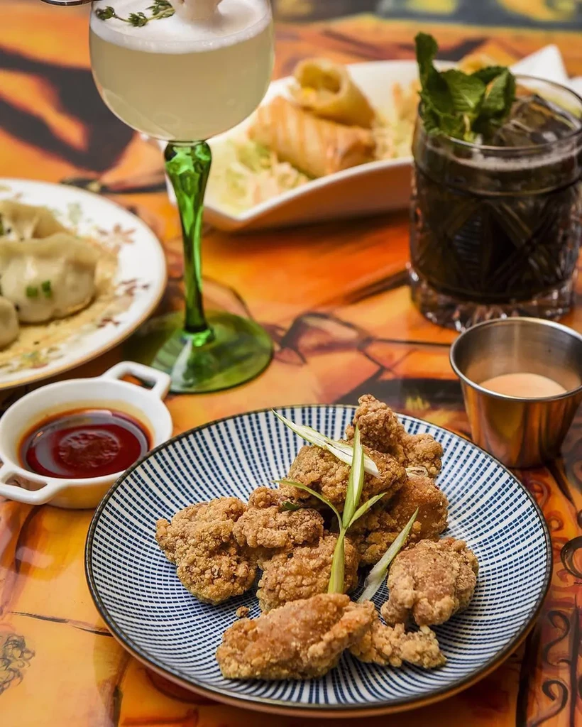 Restaurant table with fried chicken, dumplings, spring rolls, and cocktails.