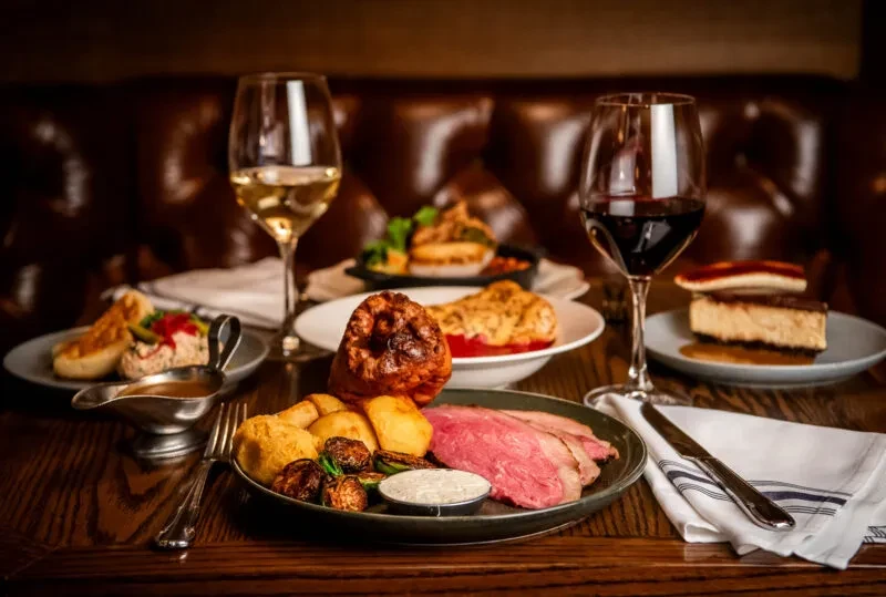 Restaurant table with roast beef dinner, appetizers, dessert, and wine.